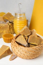 Different natural beeswax blocks and jar of honey on white wooden table