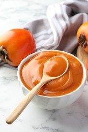 Photo of Delicious persimmon jam and fresh fruits on white marble table