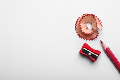 Red pencil, wooden shaving and sharpener on white background, top view