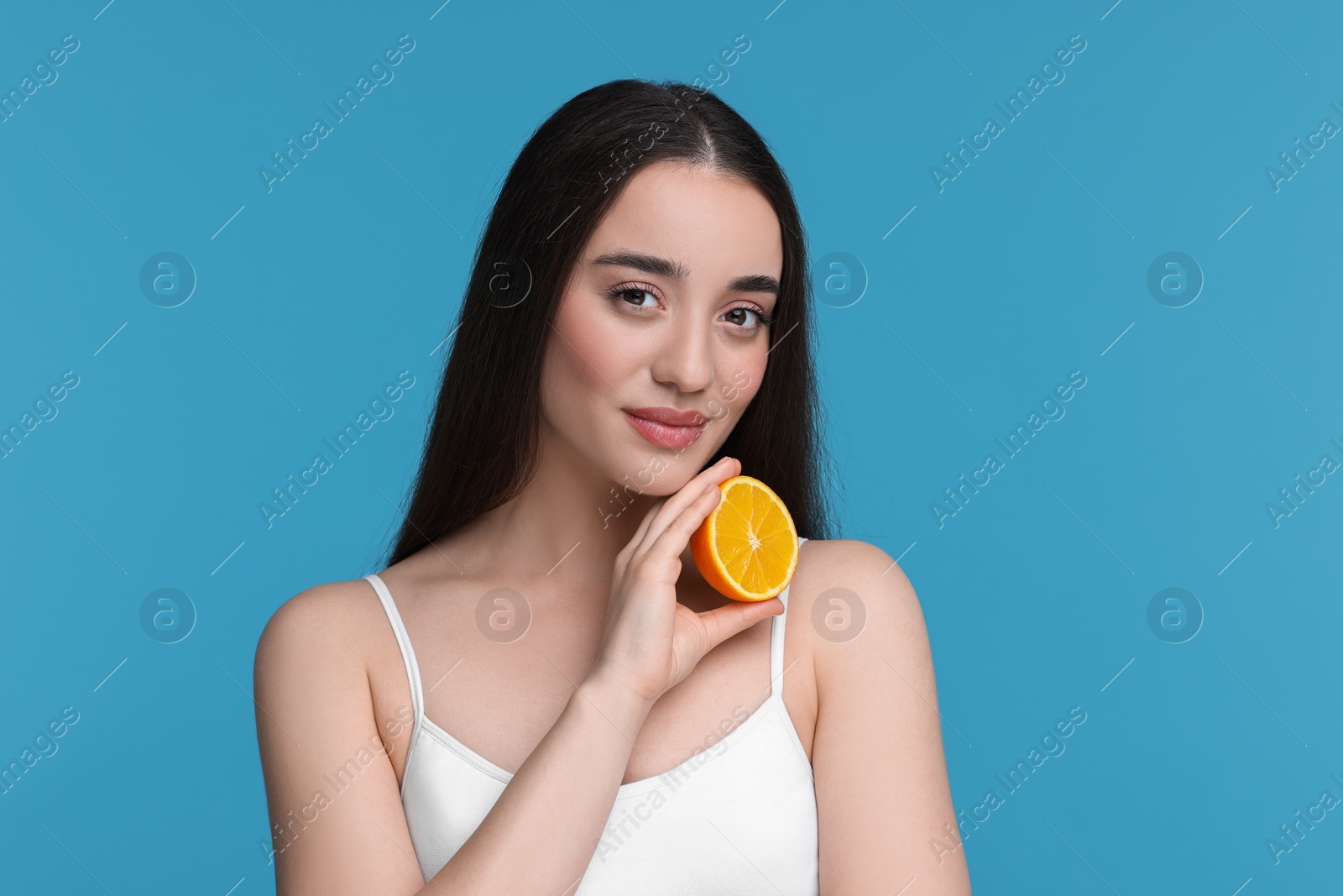 Photo of Beautiful young woman with piece of orange on light blue background