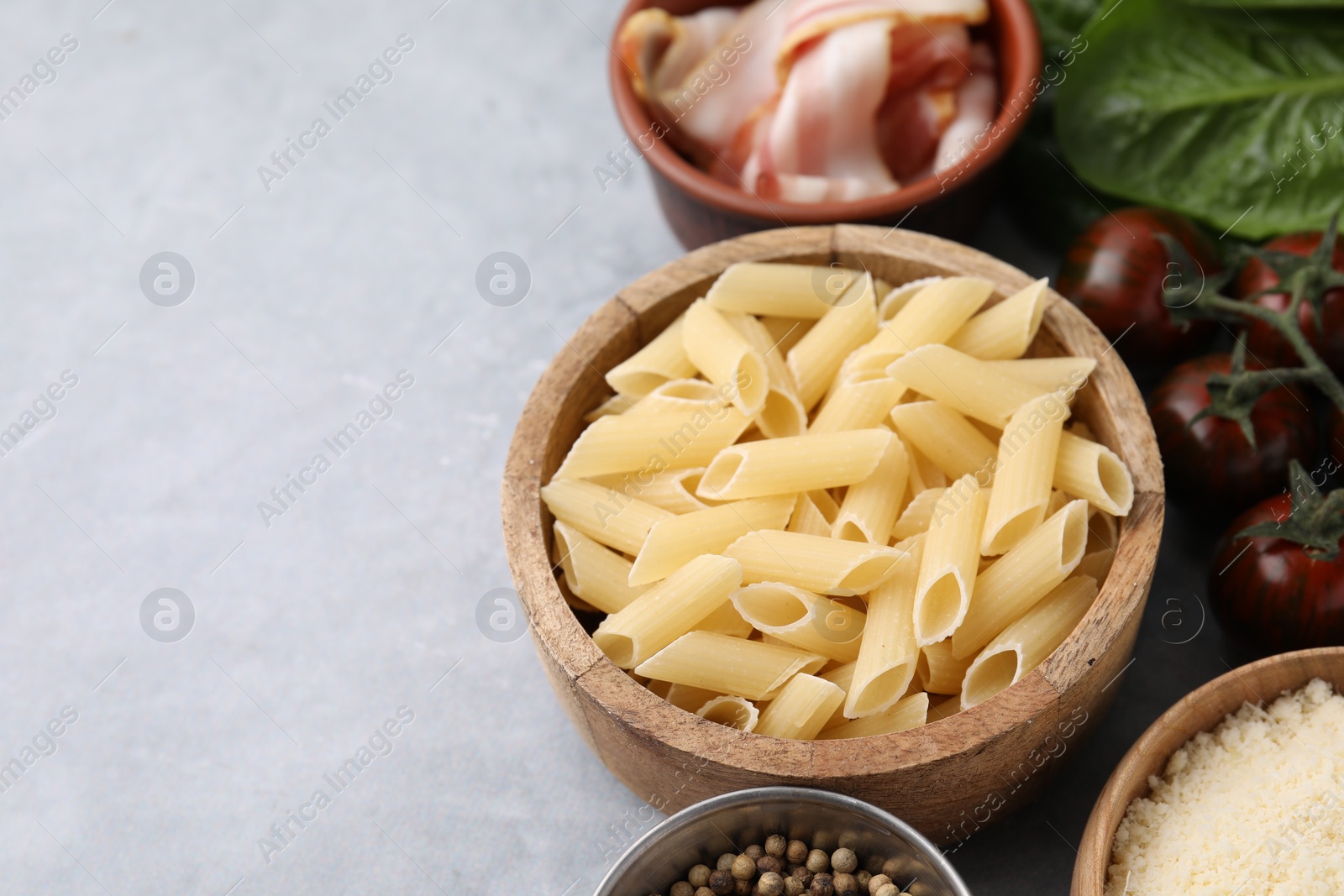 Photo of Raw pasta, bacon and fresh ingredients on light grey table, space for text