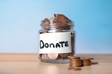 Photo of Glass jar with money and label DONATE on table against color background
