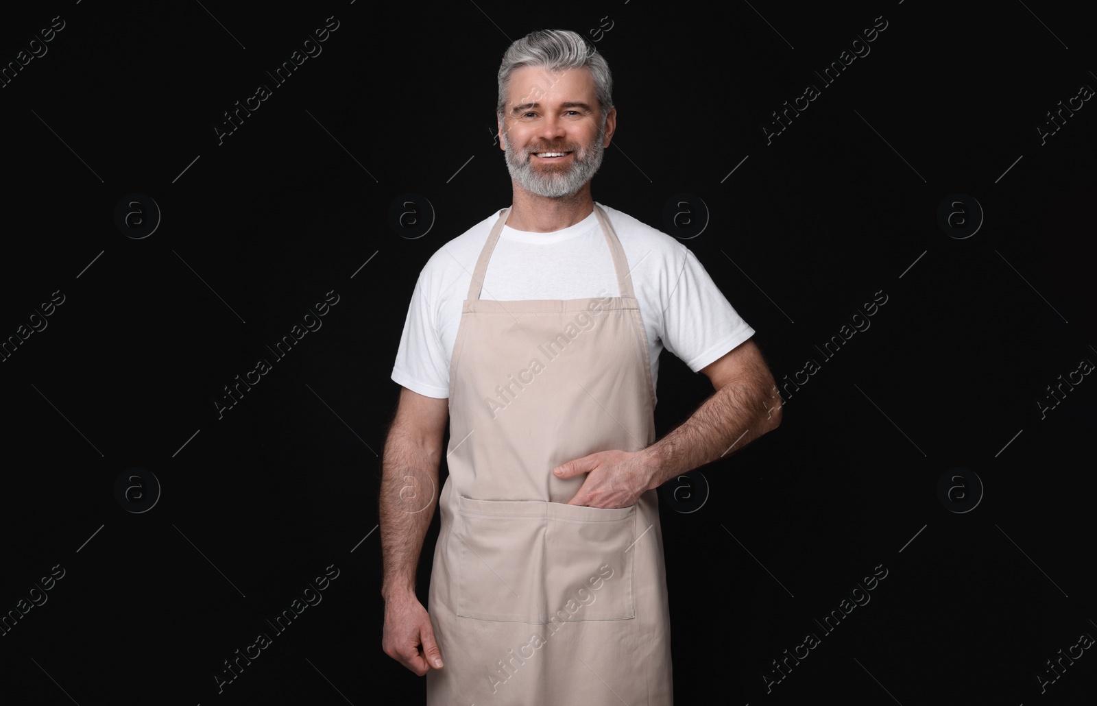 Photo of Happy man wearing kitchen apron on black background. Mockup for design