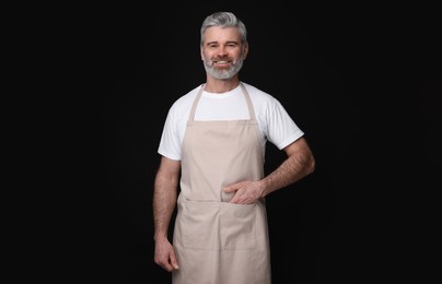 Photo of Happy man wearing kitchen apron on black background. Mockup for design