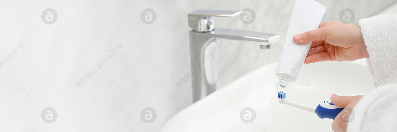 Image of Woman squeezing toothpaste from tube onto electric toothbrush above sink in bathroom, closeup. Banner design with space for text