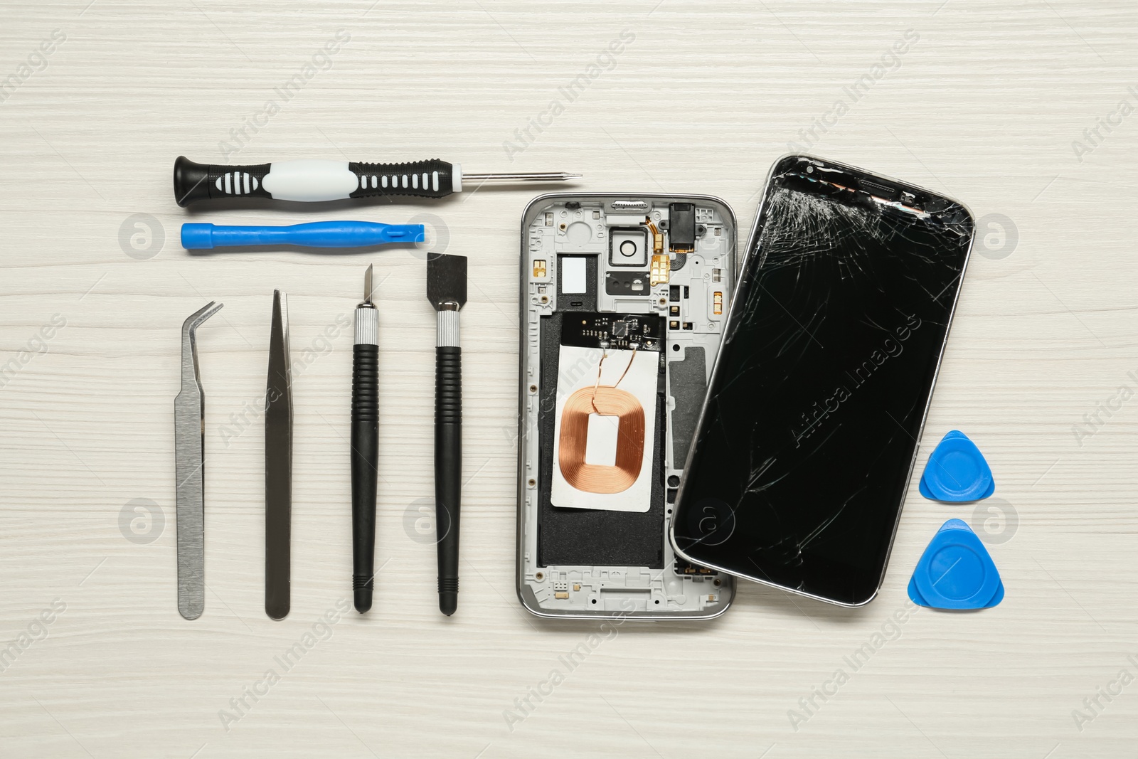 Photo of Damaged smartphone and repair tool set on white wooden background, flat lay