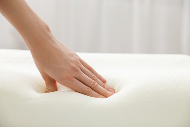 Woman touching orthopedic memory foam pillow indoors, closeup. Space for text