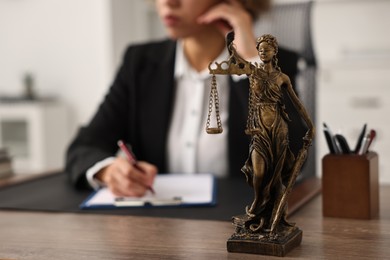 Notary with clipboard writing notes at workplace in office, focus on statue of Lady Justice