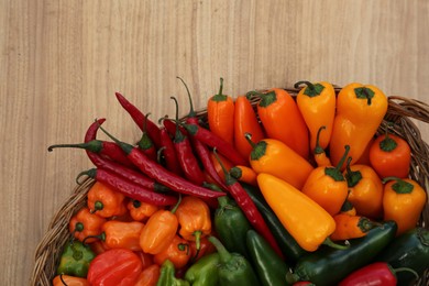 Wicker basket with many different fresh chilli peppers on wooden table, top view. Space for text