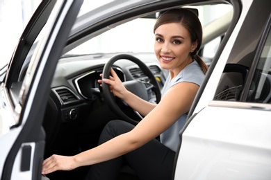 Young woman sitting in driver's seat of new car at salon