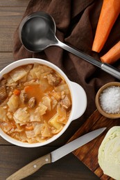 Photo of Tasty cabbage soup and ingredients on wooden table, flat lay