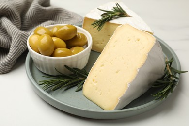 Photo of Plate with pieces of tasty camembert cheese, olives and rosemary on white table, closeup