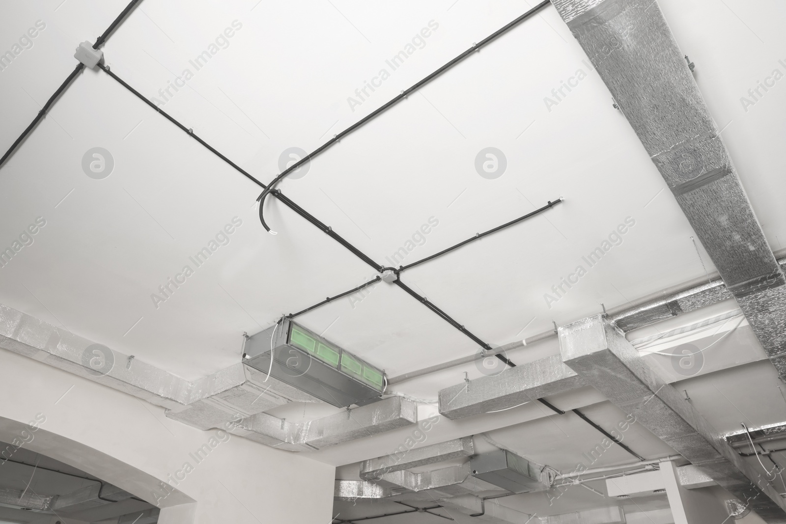 Photo of Conduits with cables and ventilation system on white ceiling, low angle view. Installation of electrical wiring