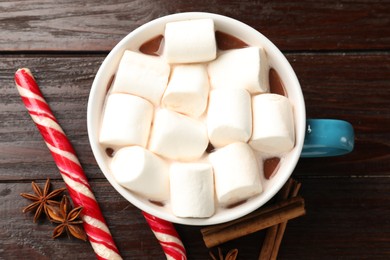 Photo of Tasty hot chocolate with marshmallows, candy cane and spices on wooden table, flat lay