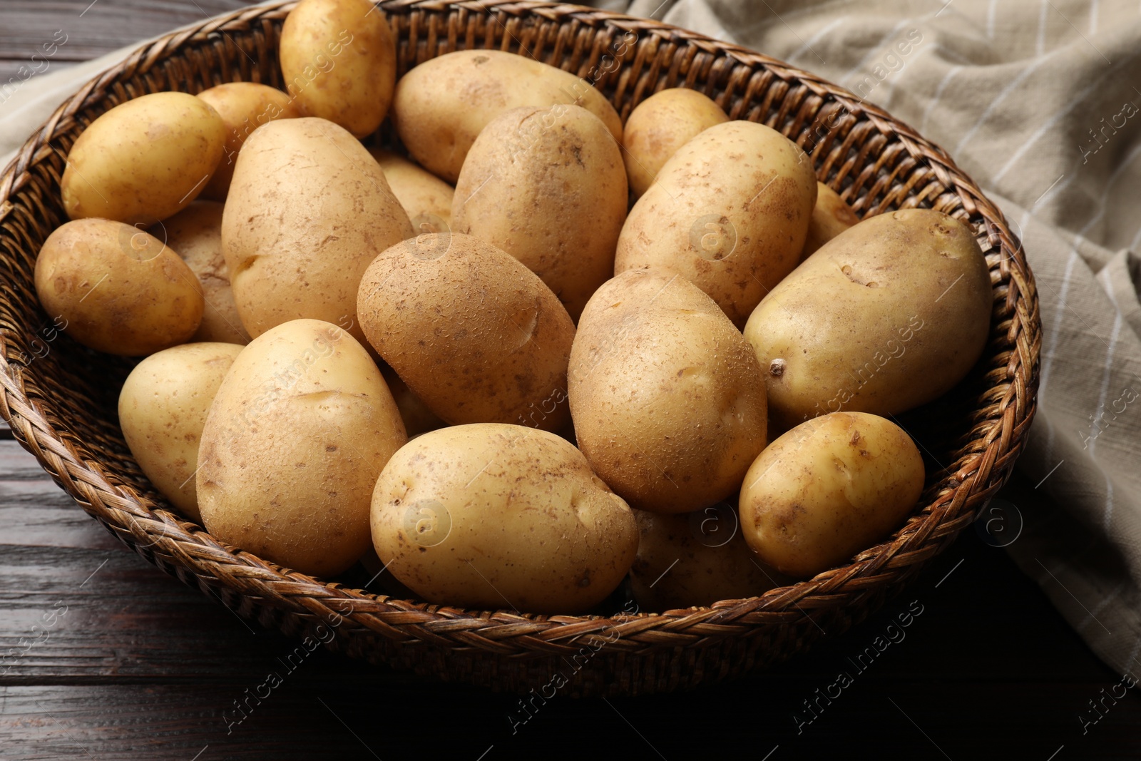 Photo of Raw fresh potatoes in wicker basket on wooden table