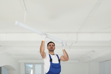 Photo of Electrician installing led linear lamp indoors. Ceiling light