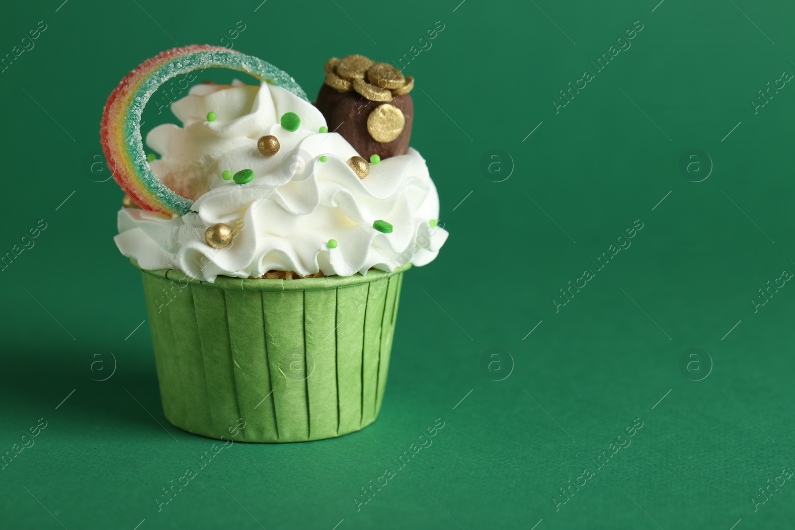 Photo of St. Patrick's day party. Tasty cupcake with sour rainbow belt and pot of gold toppers on green background, closeup. Space for text