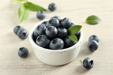 Photo of Bowl of fresh tasty blueberries on white wooden table, closeup