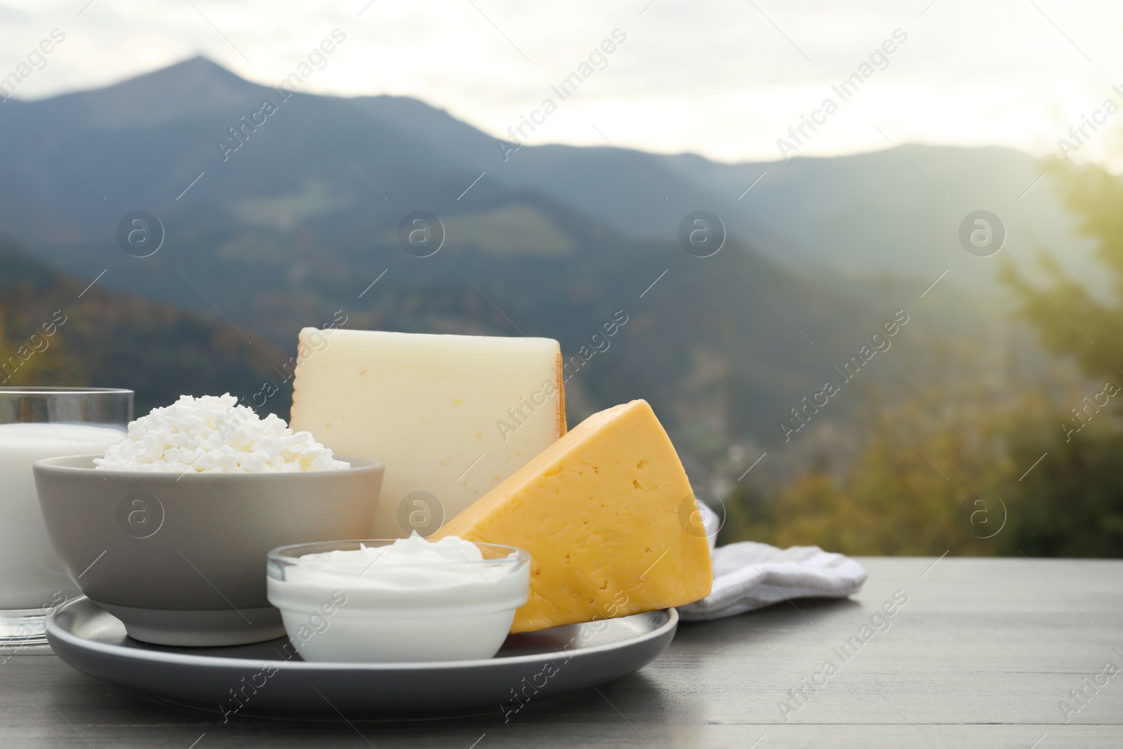 Photo of Tasty cottage cheese and other fresh dairy products on grey wooden table in mountains. Space for text