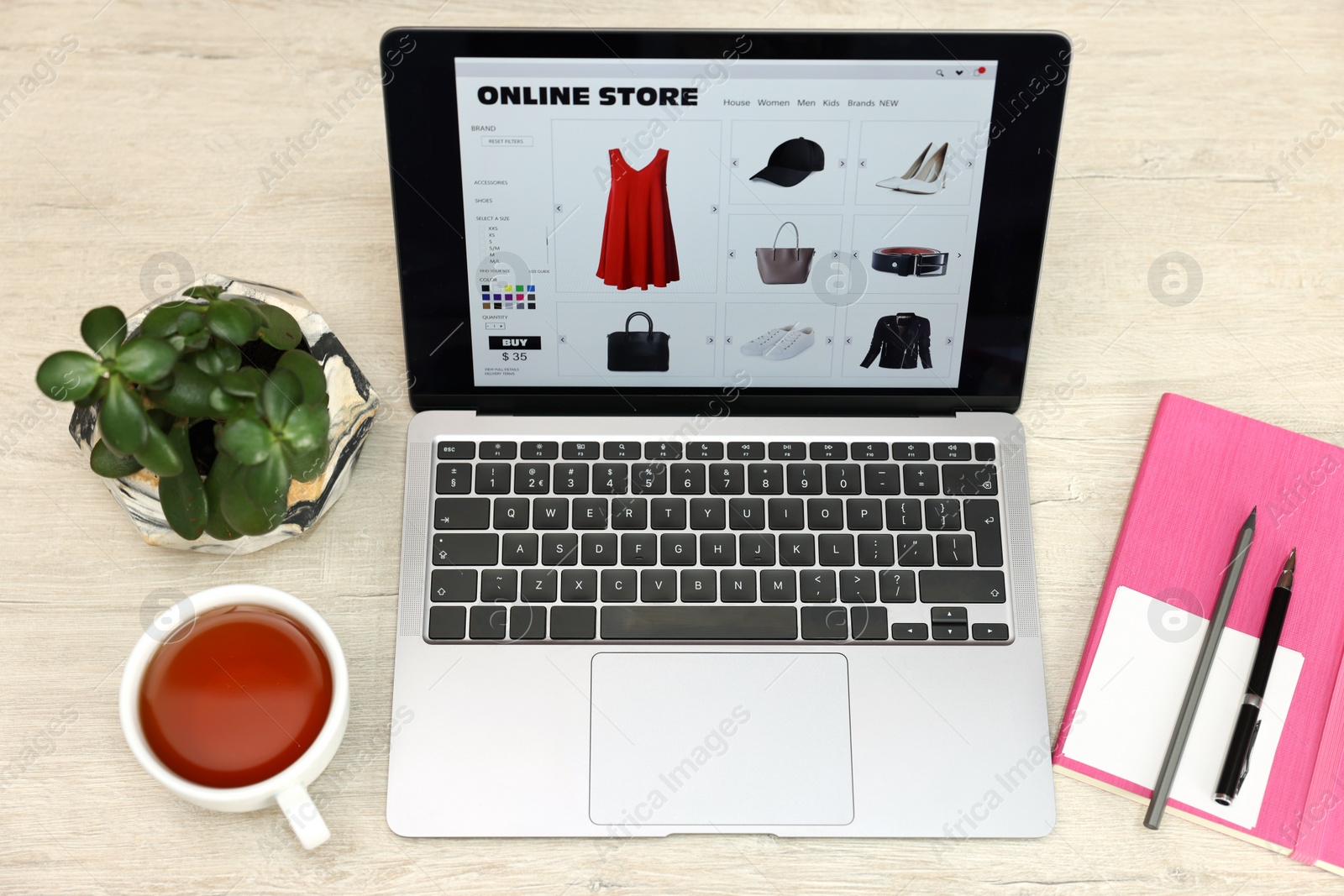 Photo of Online store. Laptop with open website, notebook, pen and pencil on wooden table, above view