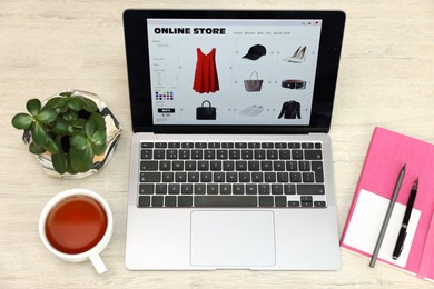 Photo of Online store. Laptop with open website, notebook, pen and pencil on wooden table, above view