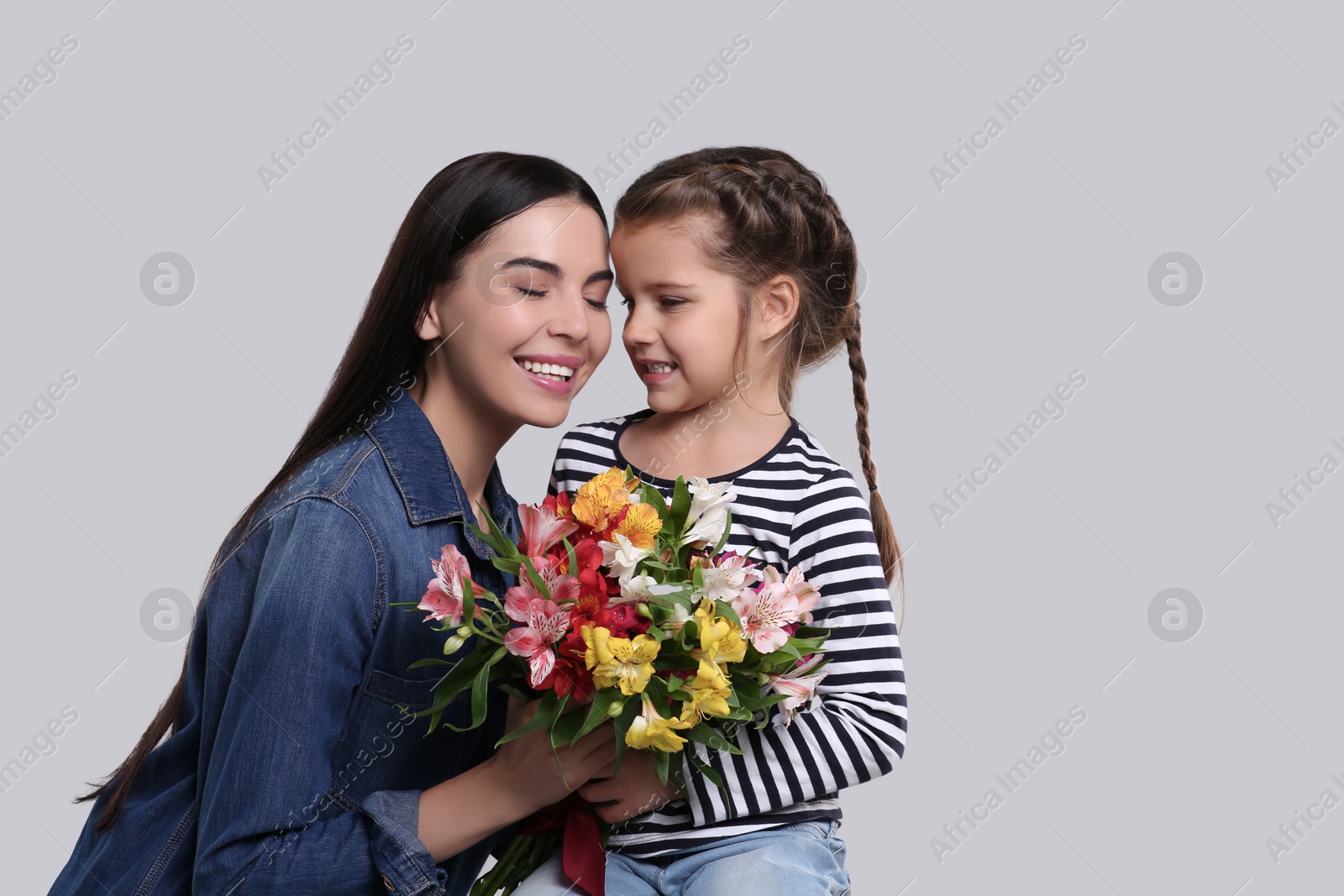 Photo of Happy woman with her cute daughter and bouquet of beautiful flowers on light grey background. Mother's day celebration