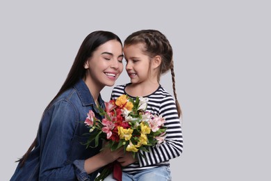 Happy woman with her cute daughter and bouquet of beautiful flowers on light grey background. Mother's day celebration