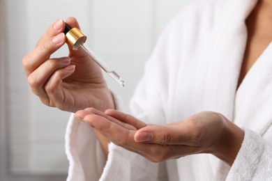 Woman applying cosmetic serum onto her hand on light background, closeup