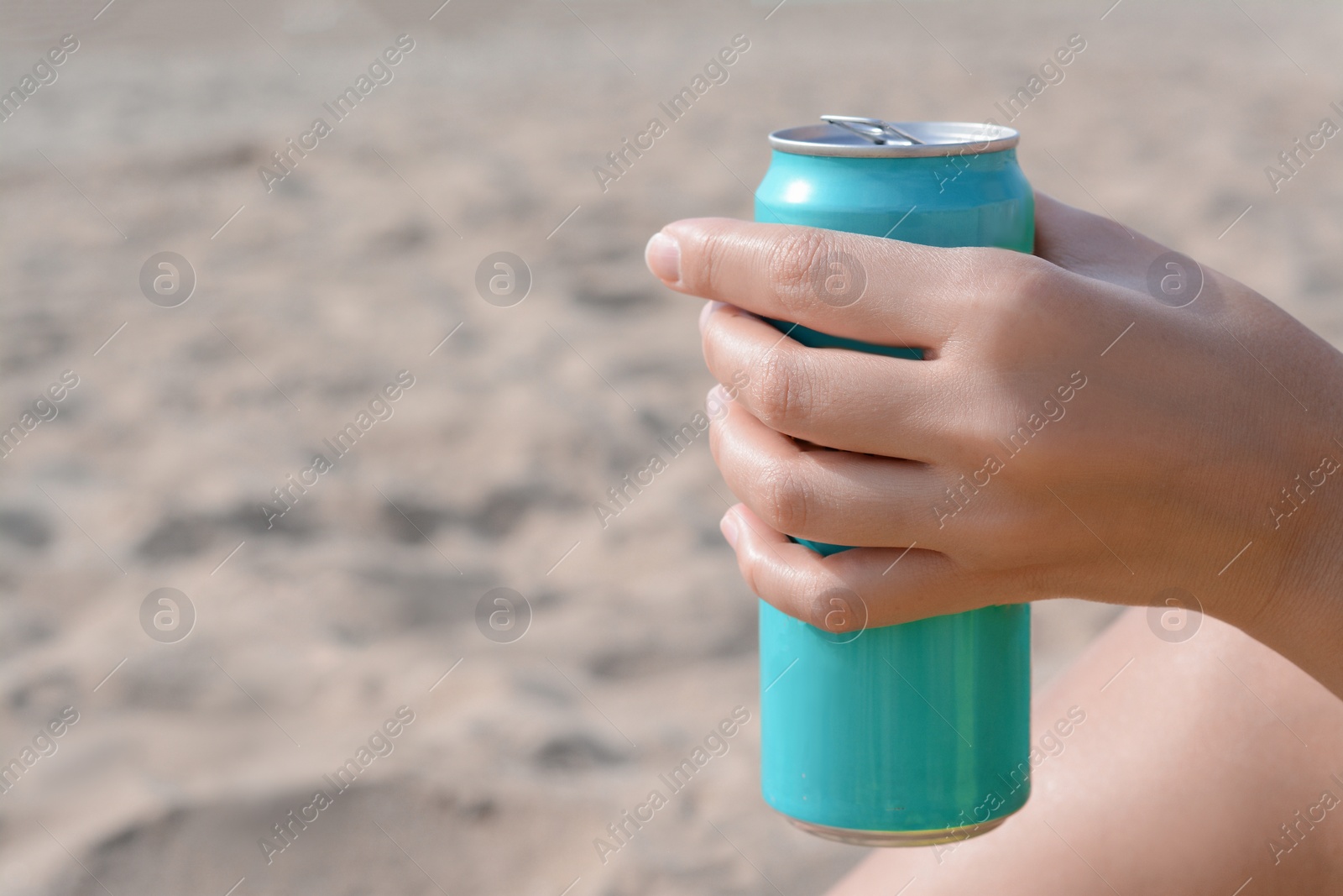 Photo of Woman holding aluminum can with beverage on sand, closeup. Space for text