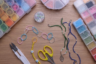 Photo of Beautiful handmade beaded jewelry and supplies on wooden table, flat lay