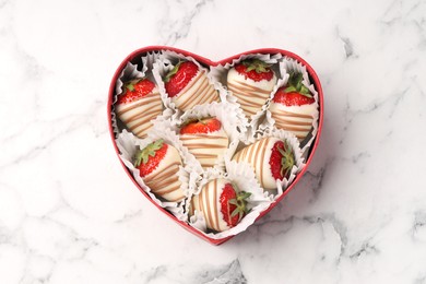 Heart shaped box with delicious chocolate covered strawberries on white marble table, top view