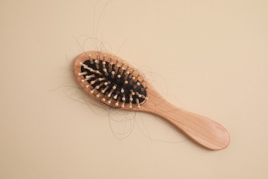 Wooden brush with lost hair on beige background, top view