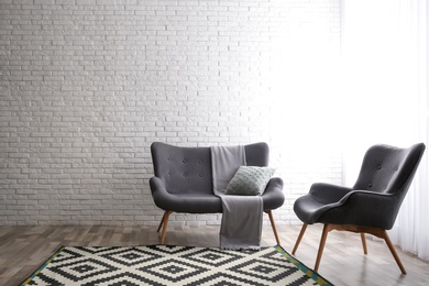 Photo of Stylish sofa and armchair near brick wall in modern living room interior. Space for text