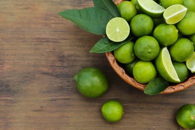 Whole and cut fresh ripe limes in bowl on wooden table, flat lay. Space for text