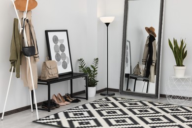 Photo of Stylish hallway room interior with bench, shoes, clothes rack and floor mirror