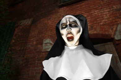 Photo of Portrait of scary devilish nun outdoors, space for text. Halloween party look