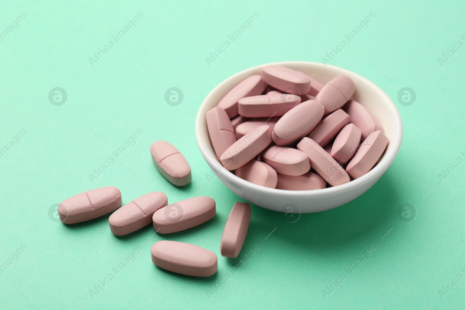 Photo of Pink vitamin capsules and bowl on turquoise background