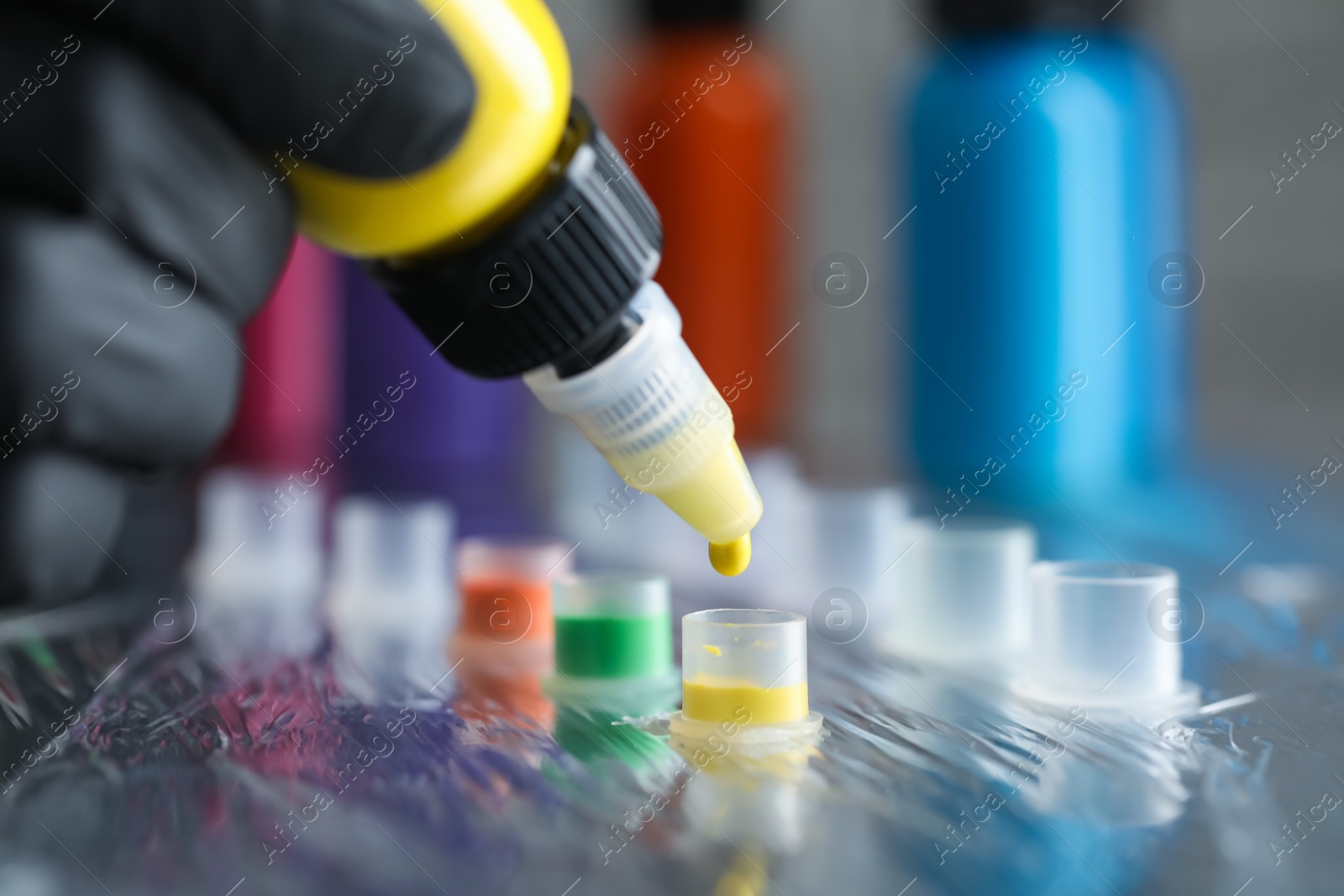 Photo of Tattoo artist dripping yellow tattoo ink into cap on table, closeup