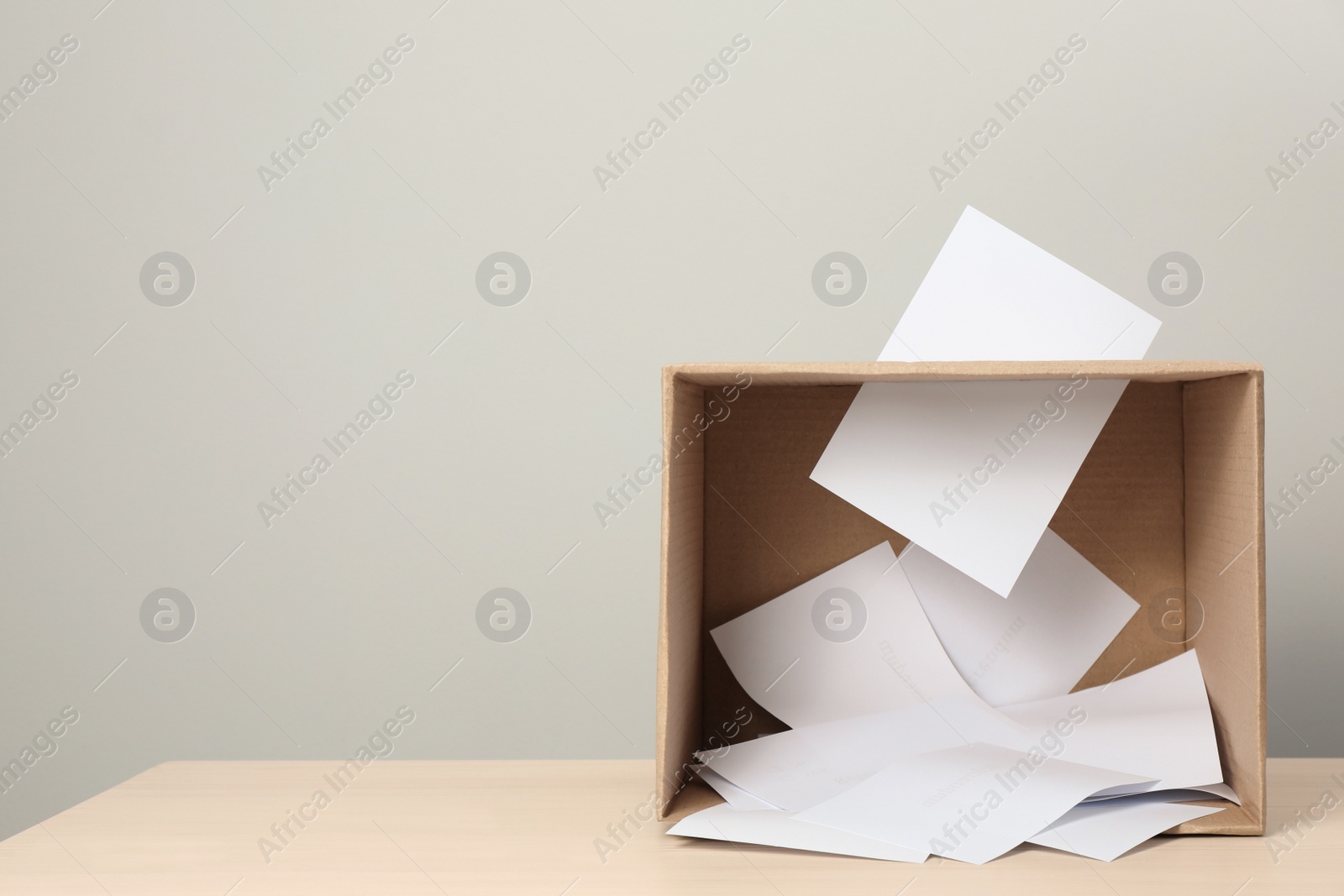 Photo of Ballots in box on table against light grey background. Space for text