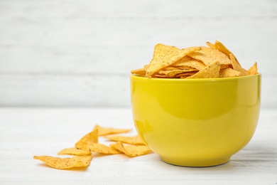 Yellow bowl with tasty Mexican nachos chips on white wooden table, space for text