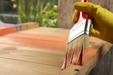 Photo of Worker applying coral paint onto wooden surface against blurred background, closeup. Space for text