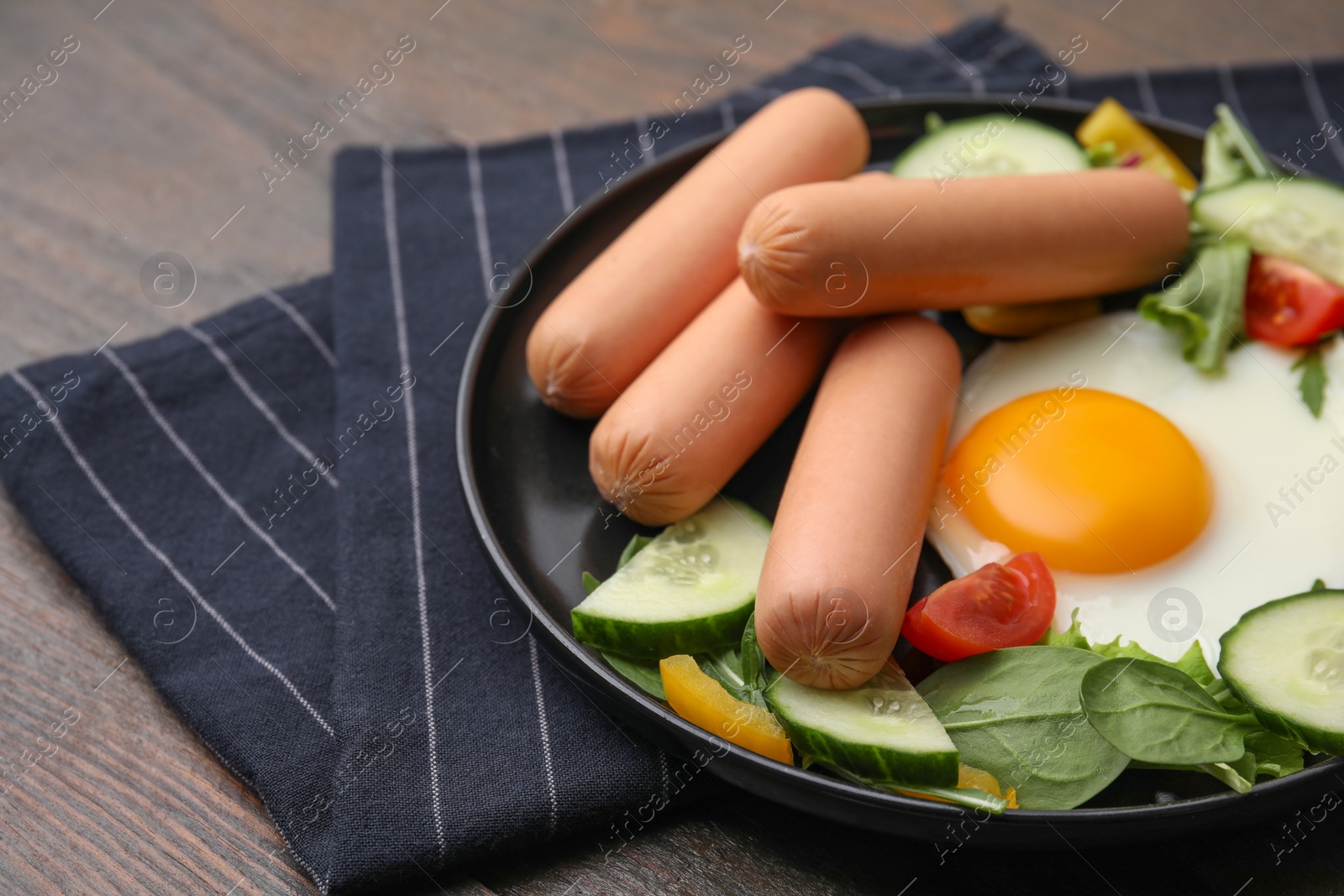 Photo of Delicious breakfast with boiled sausages and fried egg on wooden table, closeup