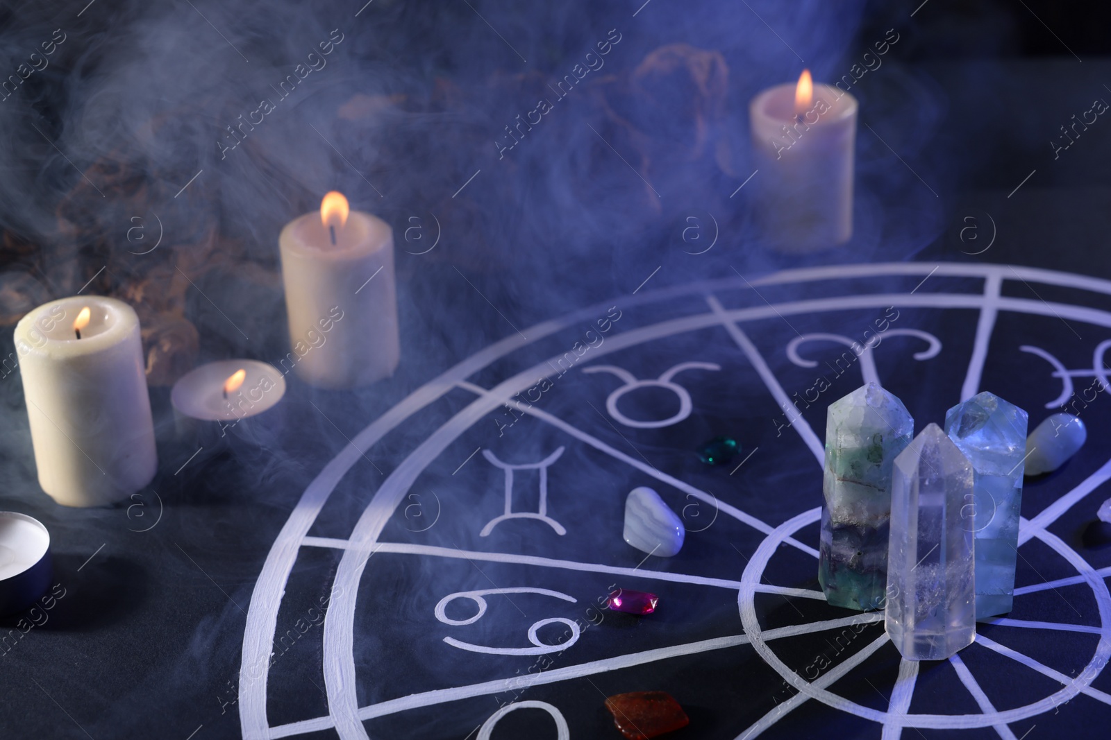 Photo of Natural stones for zodiac signs, drawn astrology chart and burning candles on black table. Color tone effect