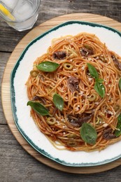 Photo of Delicious pasta with anchovies, tomato sauce and basil on wooden table, top view