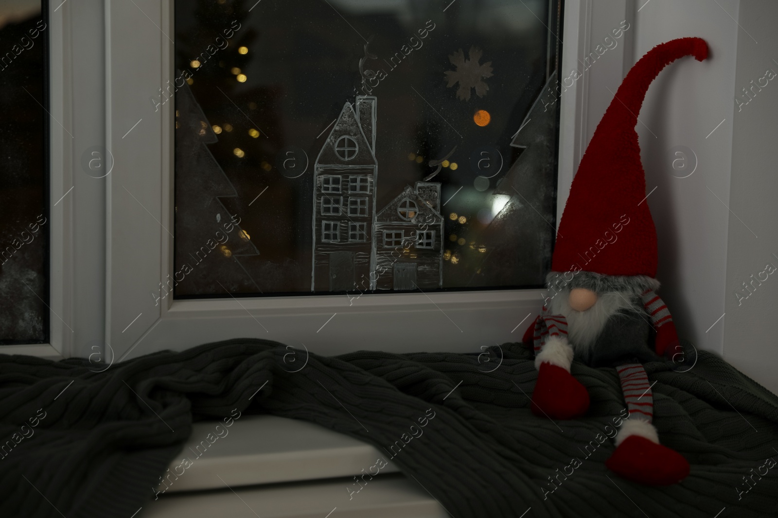 Photo of Gnome and plaid near window with beautiful drawing at home. Christmas decor