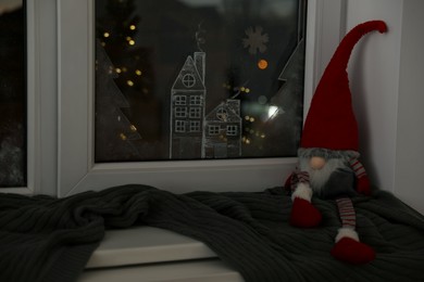 Photo of Gnome and plaid near window with beautiful drawing at home. Christmas decor