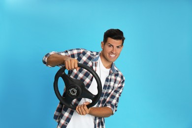 Photo of Happy man with steering wheel on light blue background