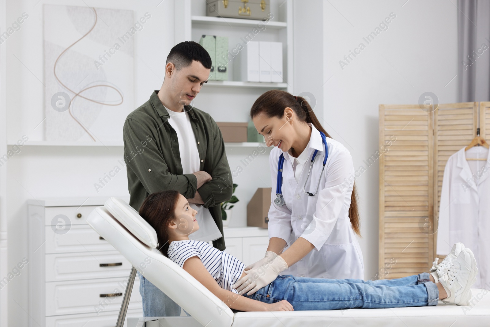 Photo of Gastroenterologist examining girl with stomach ache on couch in clinic