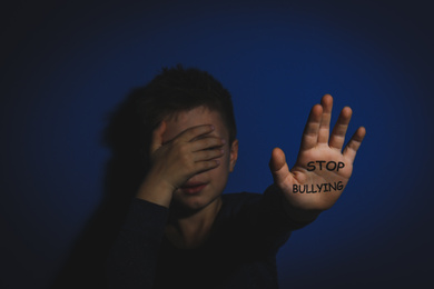 Image of Abused little boy showing palm with message STOP BULLYING near blue wall, focus on hand