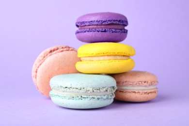 Photo of Pile of delicious colorful macarons on violet background, closeup